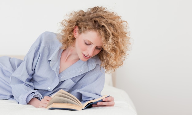 Красивая блондинка женщина, чтение книги, лежа на кровати