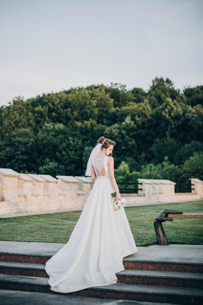 Gorgeous bride in amazing gown walking in evening park bride in stylish dress posing with bouquet back view