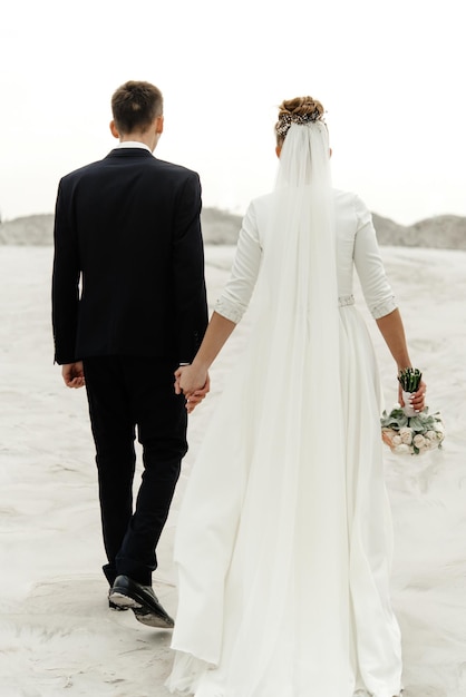 Gorgeous bride and groom walking holding hands and looking ar each other at sandy beach lake true emotions