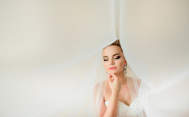 Gorgeous bride holds her hand under the chin while veil covers her