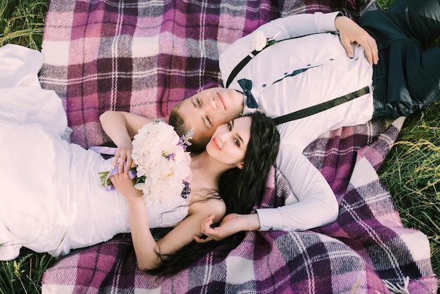 Gorgeous bride and stylish groom lying on a purple plaid Luxury wedding ceremony in a garden