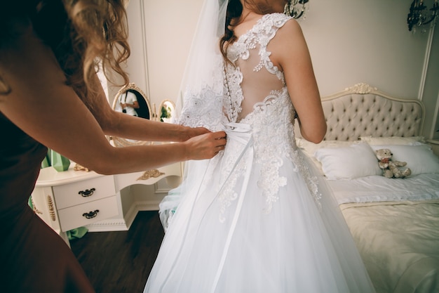 Gorgeous bride in white luxury dress is getting ready for wedding.  Woman putting on dress