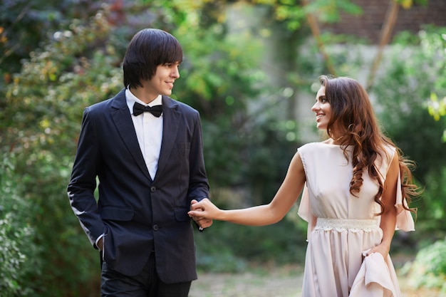 Gorgeous bride with long curly hair and bridegroom standing close to each other at green leaves background, wedding photo, looking into eyes.