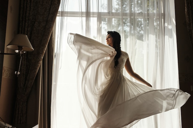 部屋の窓の前に立つゴージャスなブルネットの花嫁の渦