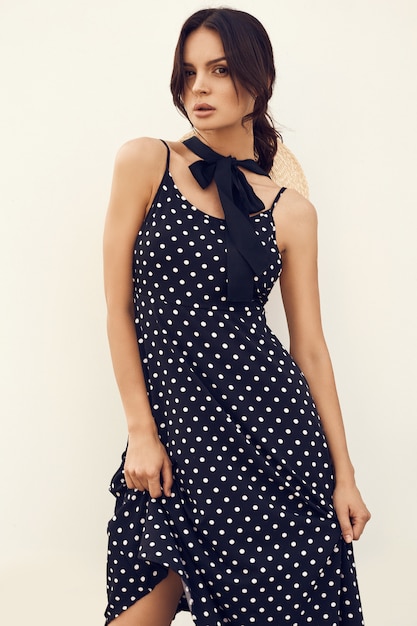 Gorgeous brunette in fashion dress with hat posing against a white wall