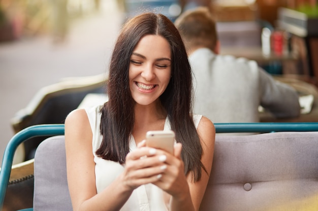 Gorgeous brunette female with happy expression using smartphone