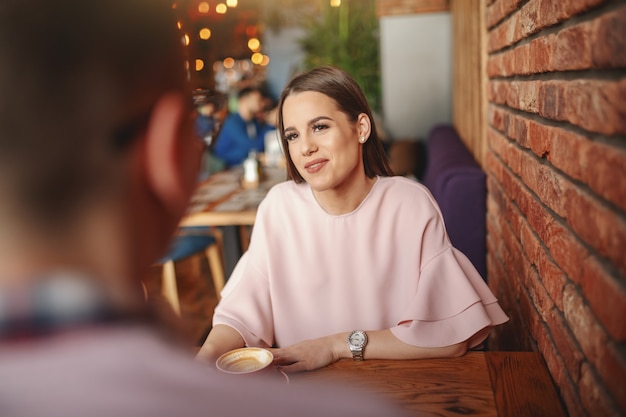 Gorgeous brunette sitting in restaurant with her boyfriend and drinking coffee