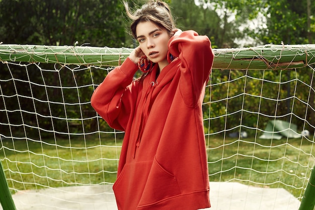 Gorgeous brunette woman in fashion red hoodie on sports field