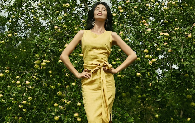 Donna splendida del brunette in vestito giallo da modo nel giardino delle mele