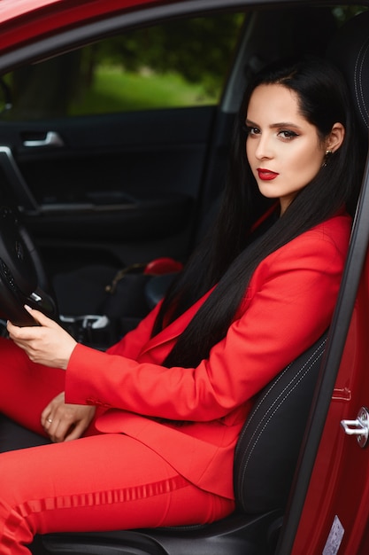 Великолепная брюнетка женщина в красном костюме в машине