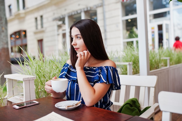 一杯のコーヒーとカフェのテーブルの上に座ってゴージャスなブルネットの女性。