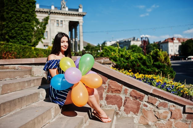 Gorgeous brunette woman at street of city with balloons at hands