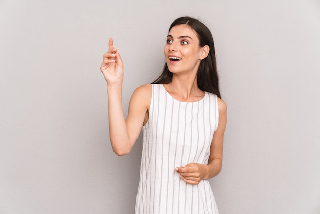  gorgeous brunette woman wearing dress smiling and looking at copyspace isolated over gray wall