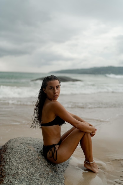 Splendida donna bruna con una figura perfetta in posa sulla spiaggia tropicale indossando eleganti costumi da bagno neri