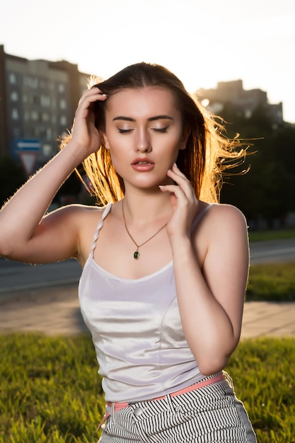 Gorgeous brunette young woman with perfect makeup posing in rays of sun at sunset