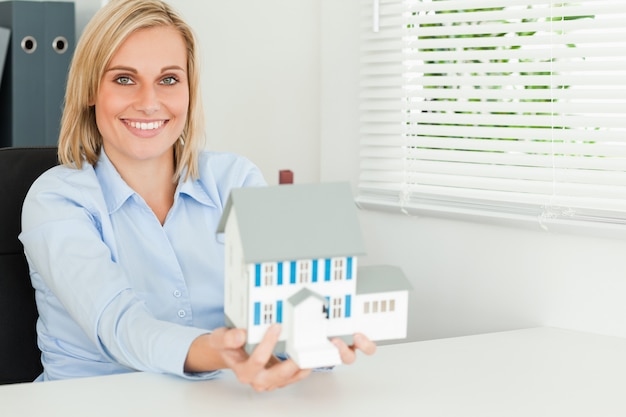 Photo gorgeous businesswoman presenting model house looks into camera