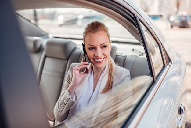 Donna di affari splendida che utilizza smartphone nell'automobile.