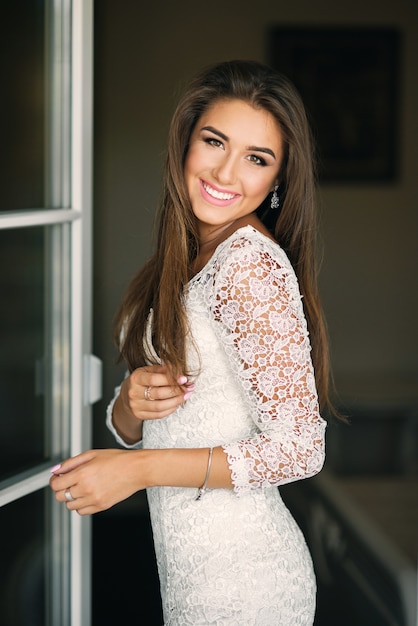 Gorgeous charming smiling bride in white lace dress withe perfect smile near the door of balcony