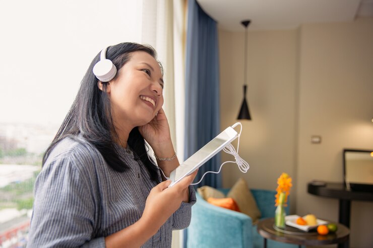 Photo タブレットやスマートフォンから音楽を聴くゴージャスな陽気なアジア女性ヘッドセット