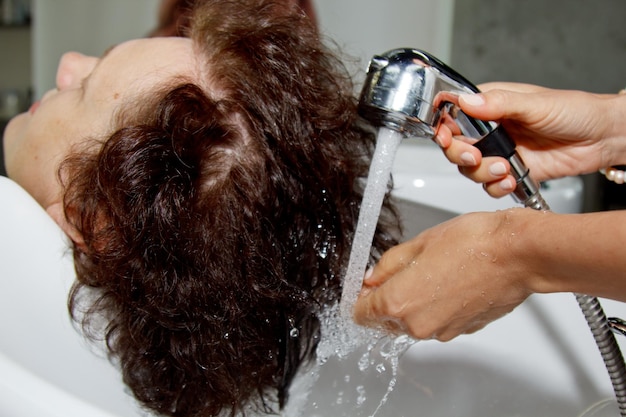 Великолепная веселая пожилая женщина наслаждается массажем головы во время мытья волос профессиональным парикмахером Уход за красотой прически модный образ жизни гламурная концепция Капли воды и пены шампуня