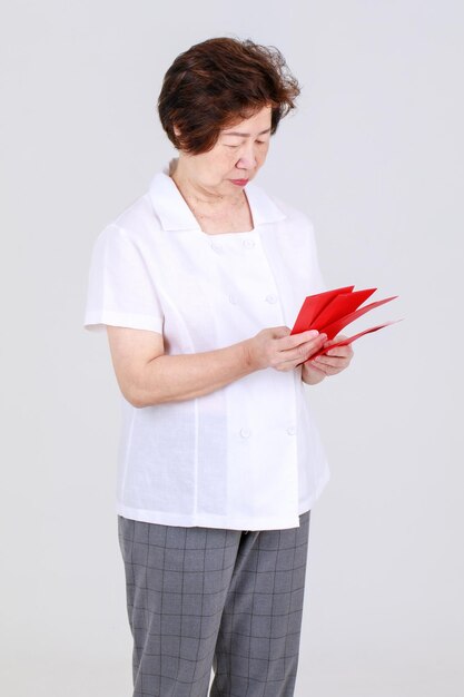 豪華な中国の年配の女性は、販売促進を提案し、休日のお祝いのための幸運な買い物の利益を享受するための広告として、新年の現金ギフトの赤い封筒を提供して喜んでいます。