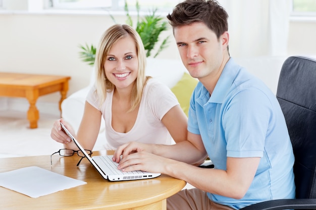 Gorgeous couple working together on the laptop sitting at a table in their living-room 
