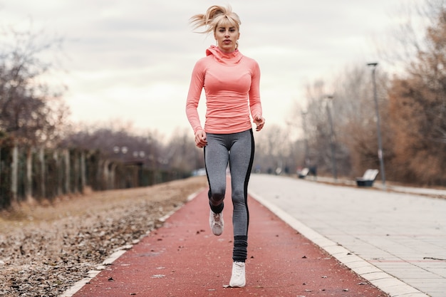 Photo gorgeous dedicated blonde caucasian woman in sportswear and with ponytail running on the racetrack.