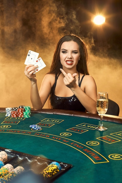 Gorgeous emotional young woman in a black dress sitting at poker table with glass of champagne. Let the smoke. Poker. Casino