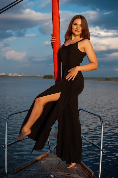 Splendida donna in forma in piedi sul ponte dello yacht e ammirando il mare al tramonto