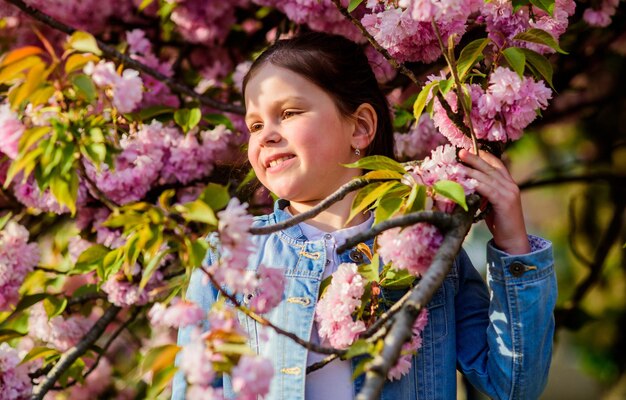 ゴージャスな花と女性の美しさ女の子の桜の背景桜の木が咲く公園と庭春の花の小さな女の子の子供が優しい花の香りをお楽しみください桜の花のコンセプト