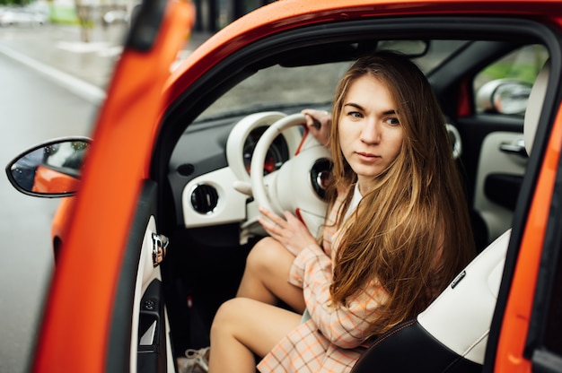 Foto ragazza splendida con capelli lunghi che si siedono in un'automobile elettrica rossa