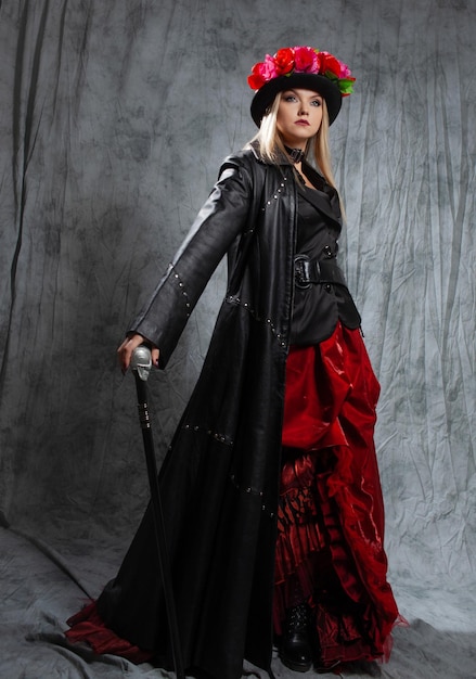 Gorgeous gothic lady in a long leather coat and a hat with roses uses a cane