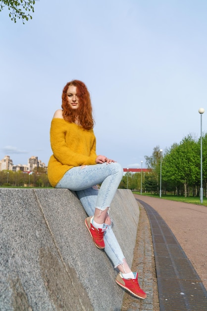 Gorgeous happy redhead woman sitting on beaton and grass relaxing in local park