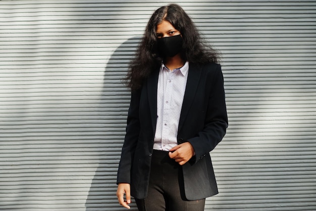 Gorgeous indian woman wear formal and black face mask posing against wall during covid pandemia