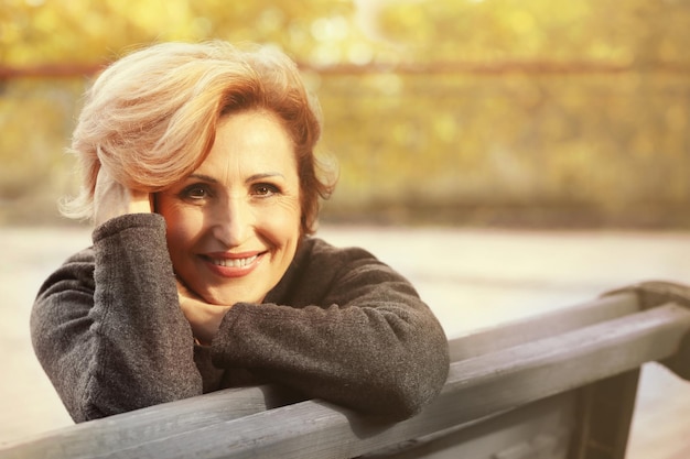 Gorgeous middle aged woman sitting on bench in autumn park