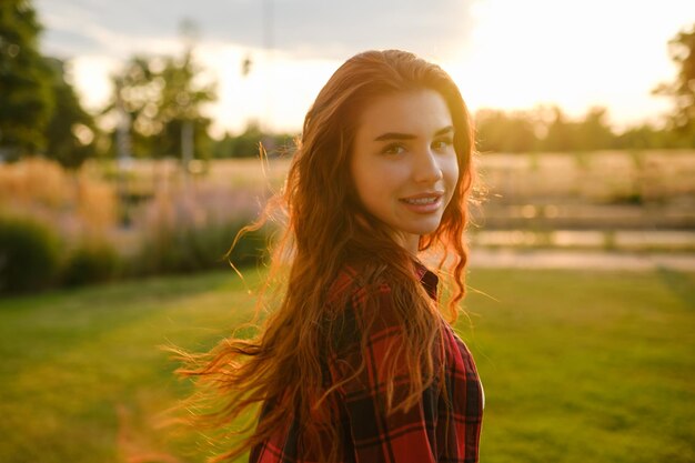 Gorgeous red haired woman stands in the park and her hair flutters in the wind