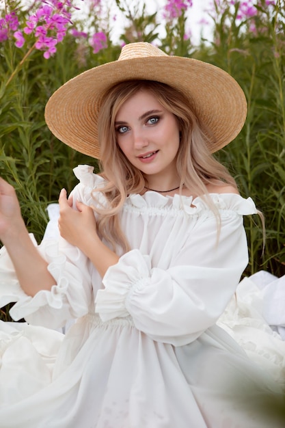 Una splendida giovane donna romantica con un vestito bianco chiaro e un cappello di paglia