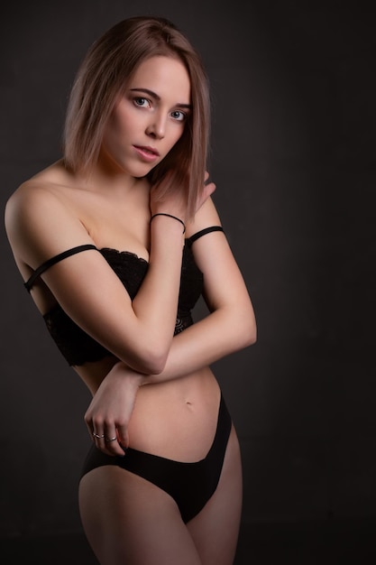 Великолепная сексуальная блондинка в черном нижнем белье позирует в студии