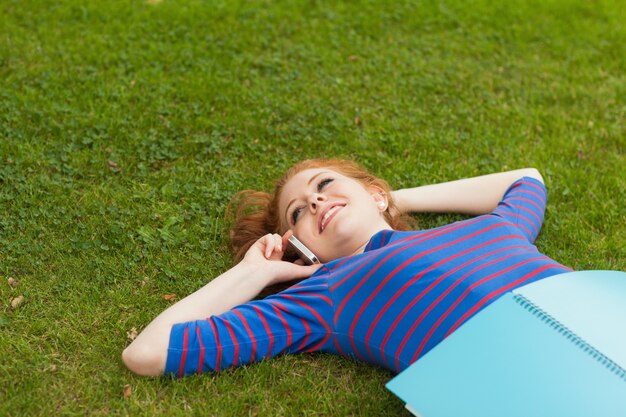 Foto studente sorridente splendido che si trova sull'erba che telefona