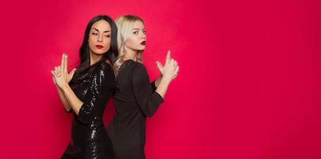 A gorgeous smiling young brunette woman and blonde woman in trendy stylish dresses are posing together and having fun isolated in the studio Friendship