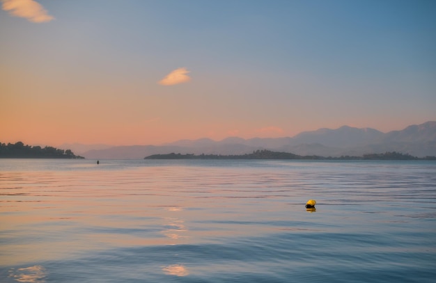 Великолепное закатное небо над морем, избирательный фокус на желтом буе Силуэты ряда островов и гор на горизонте Идея для фона или экранов Красота природы во время отпуска