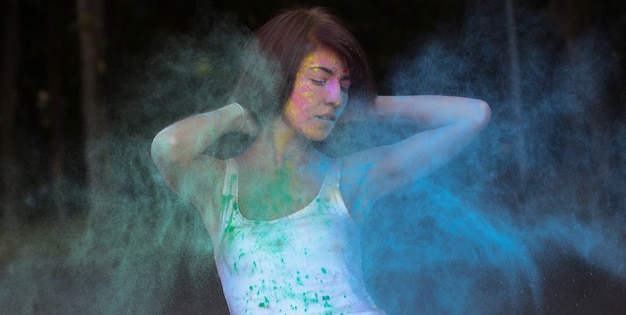 Gorgeous tanned woman with short hair posing with exploding Holi blue and green dry paint