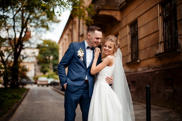 Gorgeous wedding couple walking in the city. Groom in a stylish suit and bride in a beautiful white dress