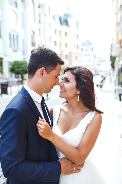 Gorgeous wedding couple walking in city Groom in stylish suit bride in beautiful white dress