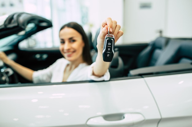 Gorgeous woman buying a new car for job and travel in dealership girl customer with key in hand