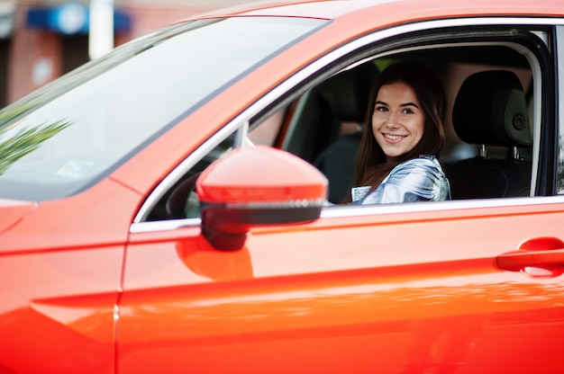 オレンジ色のSUV車を運転するゴージャスな女性