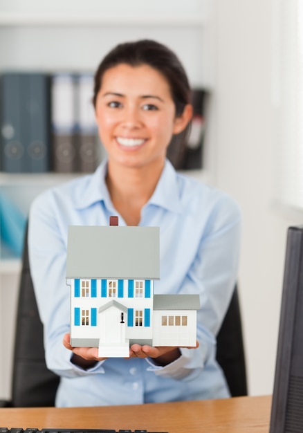 Gorgeous woman holding a miniature house while looking at the camera