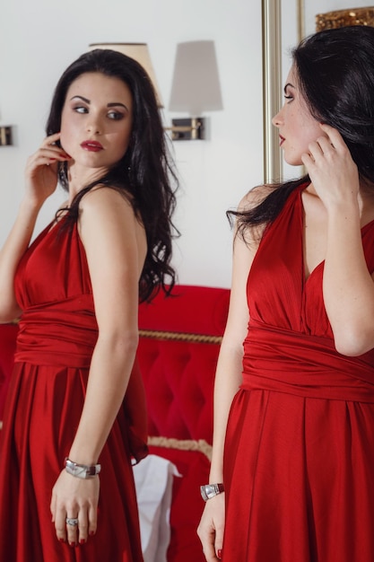 赤いドレスを着たゴージャスな女性がホテルのスイートルームに立っていますスタイリッシュなアパートと美しいブルネット