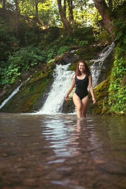 Gorgeous woman in sexy black swimsuit in front of waterfall copy space summer time