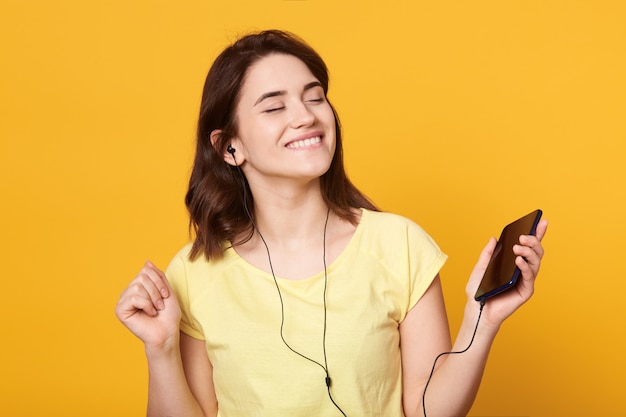 Gorgeous woman with satisfied facial expression and closed eyes listening to music